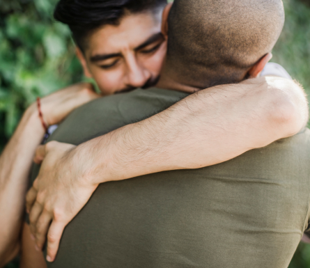Two people embracing outdoors, wearing green shirts, showing a supportive hug
