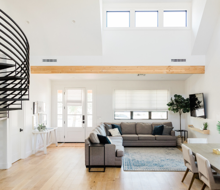 Bright, modern living room with a sectional sofa, dining area, spiral staircase, and large windows